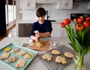 Young boy decorating Easter cookies on counter of a modern kitchen. — Stock Photo