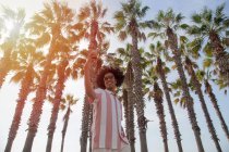 Latino in seinen Zwanzigern beim Selfie unter Palmen am Strand. Dunkelhäutiger Mann macht Selfie von sich im Stehen. — Stockfoto