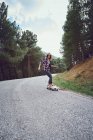 Una donna con uno skateboard su una strada di montagna — Foto stock