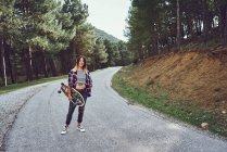 Una mujer con un monopatín en un camino de montaña - foto de stock