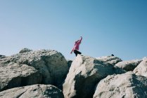 Menina correndo ao longo de grandes rochas jogando ao sol — Fotografia de Stock