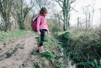 Chica fuera caminando y explorando la naturaleza con su palo en un arroyo - foto de stock