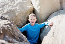 Garçon se tenait souriant dans les rochers à la plage par une journée ensoleillée au Royaume-Uni — Photo de stock