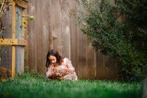 Милая маленькая девочка играет с цыпленком на цветущем заднем дворе — стоковое фото