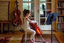 A focused graceful child practices cello in window light at home — Stock Photo
