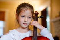 Primer plano de la linda chica enfocada practicando violonchelo en casa, - foto de stock