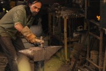 Ferreiro trabalhando um pedaço de aço com uma marreta em uma bigorna. — Fotografia de Stock