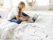 Молодая красивая женщина работает с ноутбуком в спальне — стоковое фото