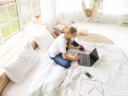 Молода красива жінка працює з ноутбуком у спальні — стокове фото