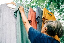 Woman hangs colorful dresses on hangers on clothesline in home garden — Stock Photo
