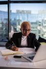Schwarze Frau benutzt Laptop und macht sich Notizen, während sie im Büro an einem Projekt arbeitet — Stockfoto