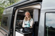 Mujer poniendo guantes de goma en su caravana de lavado felizmente - foto de stock