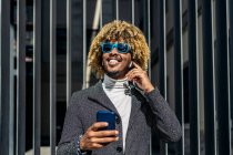 Hombre africano inteligente guapo hablando usando un teléfono móvil en la calle. Concepto de comunicación - foto de stock