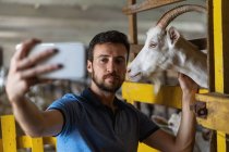 Tipo tira uma selfie ao telefone com uma cabra — Fotografia de Stock