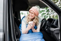 Жінка сиділа у своєму фургоні сміючись вранці з чашкою кави — стокове фото