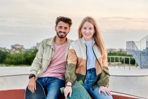 Giovane coppia multirazziale guardando la fotocamera sorridente in un parco skate — Foto stock