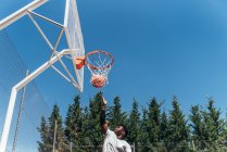 Retrato de um rapaz afro-americano a saltar para o cesto para atirar a bola. Jogando basquete em um tribunal urbano. — Fotografia de Stock