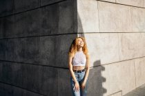 Stock photo of portrait of young blonde curly girl against the wall. She has confident attitude and looking at camera. She is wearing casual clothes — Photo de stock
