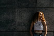 Stock photo of portrait of young blonde curly girl against the wall. She has confident attitude and looking at camera. She is wearing casual clothes — Photo de stock
