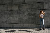 Stock photo of portrait of young blonde curly girl against the wall. She has confident attitude. She is wearing casual clothes — Photo de stock