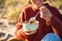 Young woman enjoying soup while beach car camping alone — Stock Photo