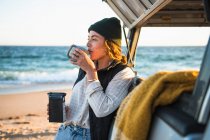 Junge Frau mit Tasse Kaffee am Strand — Stockfoto