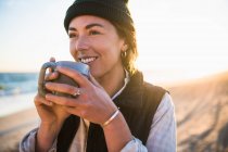 Mujer joven con taza de café en la playa - foto de stock