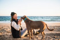 Jeune femme avec son chien boire du café sur la plage — Photo de stock