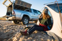 Молода жінка насолоджується кавою в подорожі кухоль в той час як пляжний автомобіль кемпінгу — стокове фото