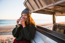 Молода жінка з чашкою п'є каву на пляжі — стокове фото