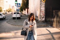 Небінарна жінка використовує смартфон під час прогулянки містом — стокове фото