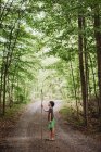 Netter Junge mit großem Wanderstock steht auf einem Pfad im Wald. — Stockfoto