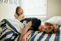 Portrait d'un garçon souriant couché par sa sœur sur son lit dans une chambre à coucher à la maison — Photo de stock