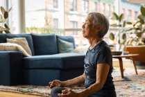 Asiatische Seniorin meditiert und entspannt zu Hause im Wohnzimmer — Stockfoto