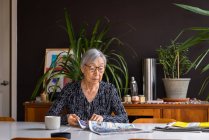 Старшая женщина читает газеты, сидя за столом с кофе — стоковое фото