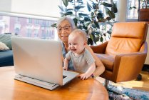Mujer mayor sentada con su nieta haciendo videollamada a través de lapto - foto de stock