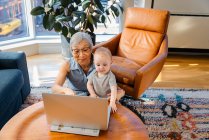 Старшая женщина сидит с внучкой и делает видеозвонок на ноутбуке — стоковое фото