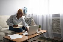 Moderne junge schwarze Angestellte in lässiger Kleidung mit Laptop und Notizbuch, während sie zu Hause im Wohnzimmer arbeitet — Stockfoto