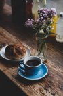 Чашка кави і квіти з булочкою на дерев'яному столі — стокове фото