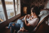 Mutter stillt Baby auf Stuhl in Vintage-Zimmer mit Blick auf den See — Stockfoto