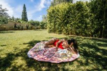 Donna che legge su un asciugamano in giardino con costume da bagno sotto un albero — Foto stock