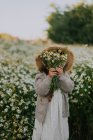 Little girl in a hat covers her face with a bouquet of daisies. — Stock Photo