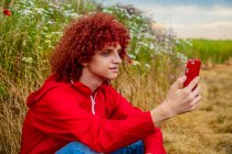 Cara jovem com cabelo encaracolado vermelho na década de 80 terno esportivo vermelho e telefone celular no exterior — Fotografia de Stock