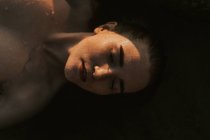 Молода жінка лежить у воді з закритими очима — стокове фото