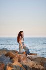 Junge rothaarige Frau blickt aufs Meer, während sie auf Felsen steht — Stockfoto