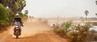 Человек на своем мотоцикле по пыльной дороге в Камбодже — стоковое фото