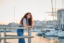Young redhead woman looks to the sea in a seaport of a city — Stock Photo