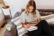 Beautiful young woman making notes at home — Stock Photo