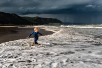 Glückliches Kind spielt am Strand mit dramatischem Himmel im Hintergrund — Stockfoto