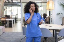 Молодая африканская американская медсестра в синей форме разговаривает по телефону и смотрит в камеру. — стоковое фото